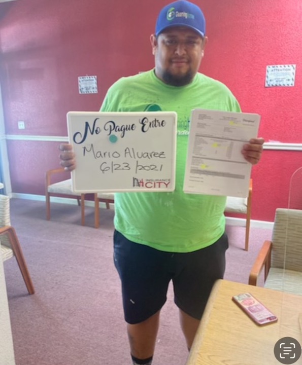 Insurance City customer holding 'No Pague Entre' card dated 2021 with auto insurance policy documents — proof no broker fee was charged