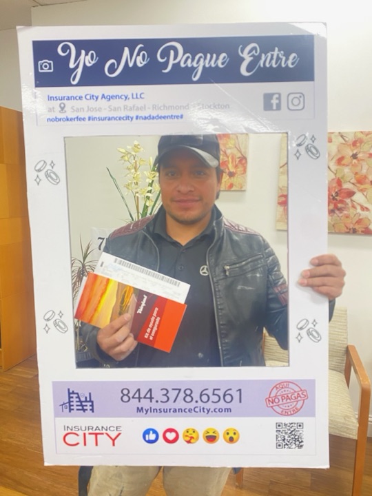 Cliente de seguro de auto en Stockton sosteniendo el marco Yo No Pagué Entré en la oficina de Insurance City Stockton